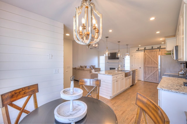 dining area featuring a barn door, recessed lighting, a notable chandelier, a fireplace, and light wood finished floors