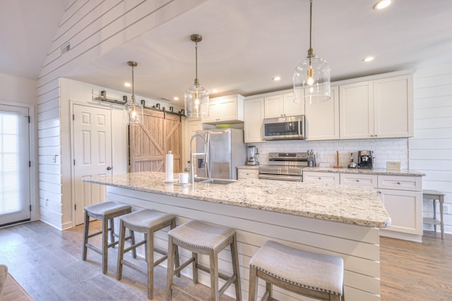 kitchen with appliances with stainless steel finishes, light wood-type flooring, an island with sink, and a barn door