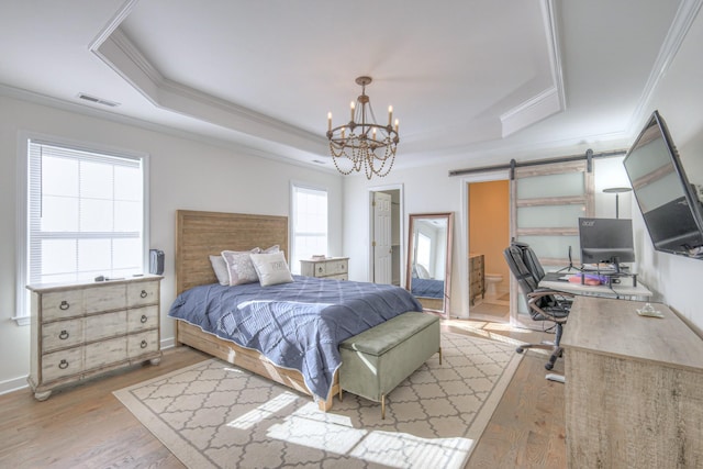 bedroom featuring a tray ceiling, visible vents, a barn door, ornamental molding, and light wood-type flooring