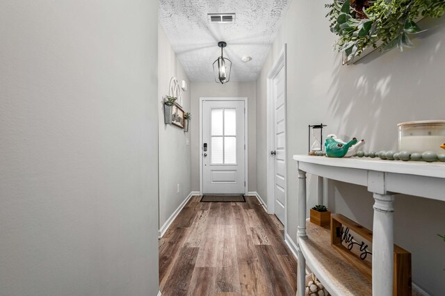 doorway featuring baseboards, a textured ceiling, visible vents, and dark wood-type flooring