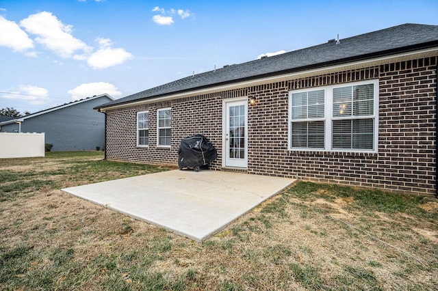 back of property with a patio area, roof with shingles, a yard, and brick siding