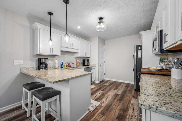 kitchen featuring a textured ceiling, stainless steel appliances, a peninsula, white cabinets, and dark wood-style floors