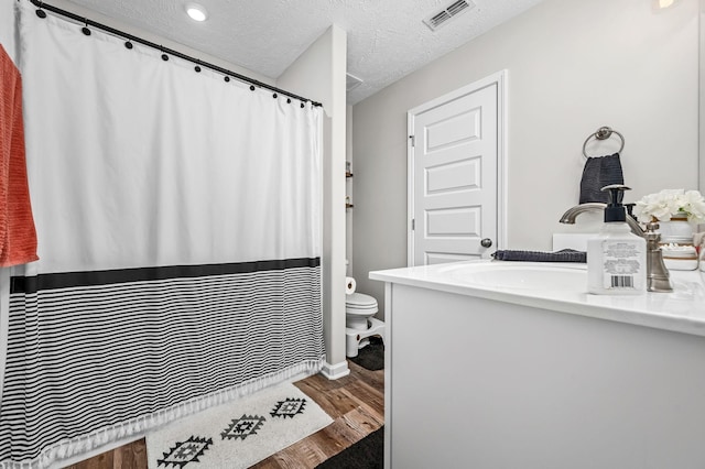 full bath with visible vents, toilet, vanity, a textured ceiling, and wood finished floors