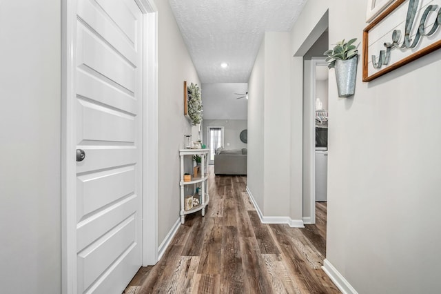 hallway featuring dark wood finished floors, a textured ceiling, and baseboards