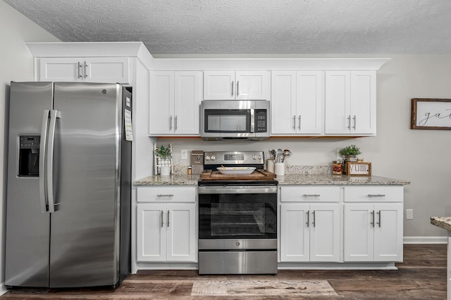 kitchen with appliances with stainless steel finishes, white cabinets, light stone counters, and dark wood-style floors