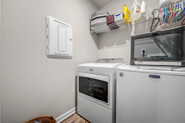 laundry area featuring laundry area, wood finished floors, baseboards, washer and dryer, and electric panel