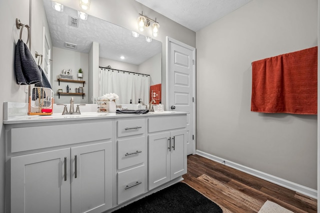 full bathroom featuring a textured ceiling, wood finished floors, a sink, baseboards, and double vanity