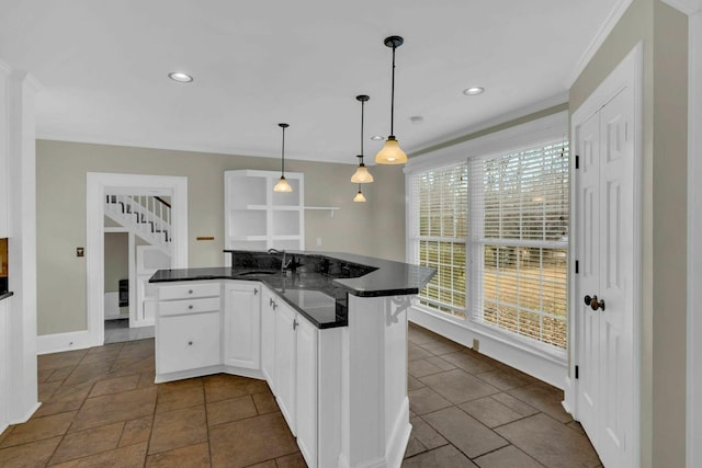 kitchen with dark countertops, ornamental molding, hanging light fixtures, white cabinetry, and a sink