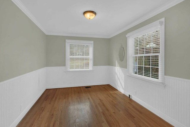 unfurnished room with a wainscoted wall, visible vents, and wood finished floors