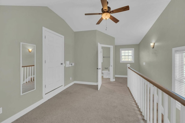 hall featuring an upstairs landing, lofted ceiling, light colored carpet, and baseboards