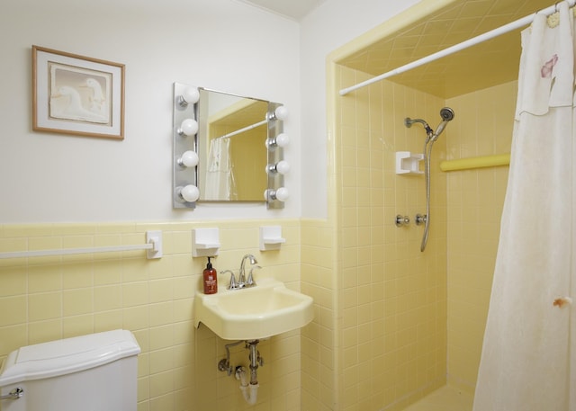 bathroom featuring tile walls, tiled shower, wainscoting, toilet, and a sink