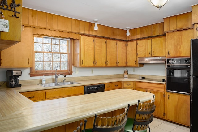 kitchen featuring a peninsula, under cabinet range hood, black appliances, a kitchen bar, and a sink