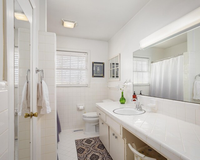 bathroom with tile walls, visible vents, toilet, vanity, and tile patterned floors