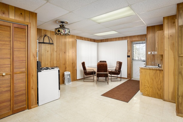 dining area featuring a drop ceiling, wood walls, and light floors