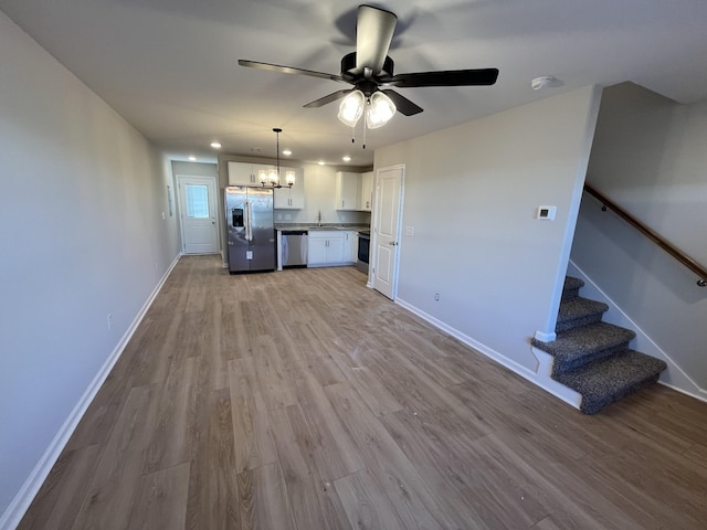 kitchen with a sink, white cabinetry, baseboards, appliances with stainless steel finishes, and light wood finished floors