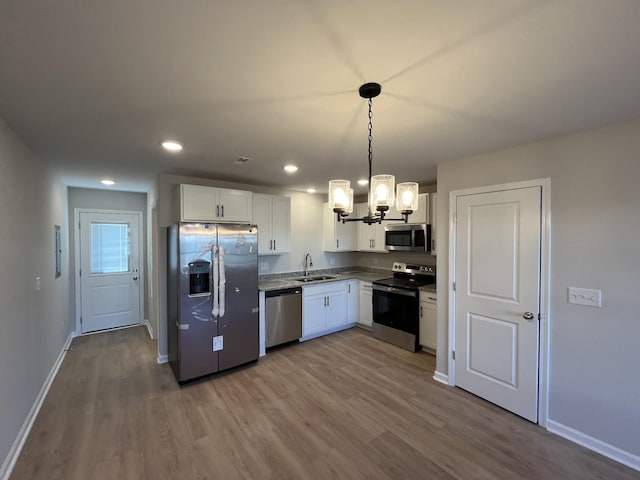 kitchen with stainless steel appliances, wood finished floors, a sink, white cabinetry, and baseboards