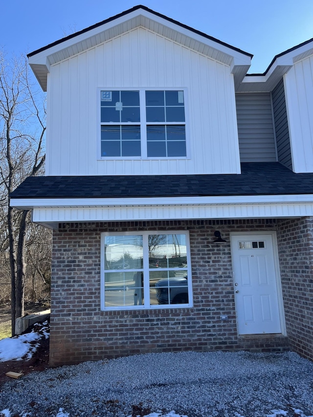 view of front facade featuring brick siding, roof with shingles, and board and batten siding