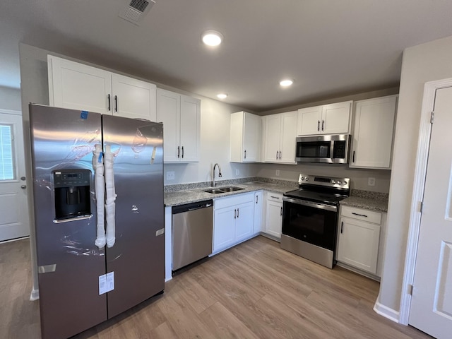 kitchen with visible vents, light wood-style flooring, appliances with stainless steel finishes, white cabinets, and a sink