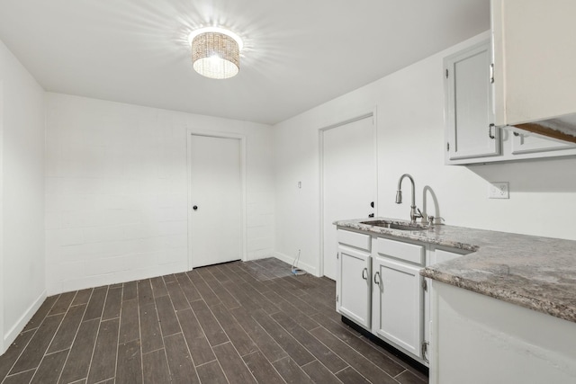 kitchen featuring dark wood-style floors, a sink, white cabinetry, and light stone countertops