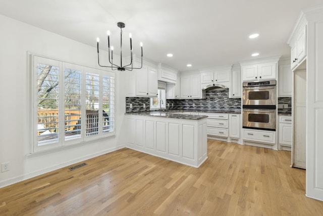 kitchen with visible vents, backsplash, double oven, light wood-style floors, and a sink