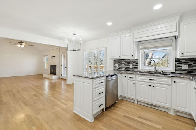 kitchen featuring a peninsula, a fireplace, white cabinetry, open floor plan, and dishwasher