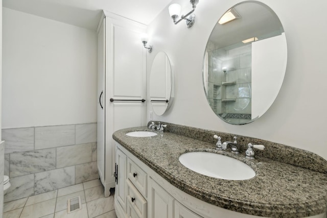 full bath with tiled shower, a sink, tile walls, and double vanity