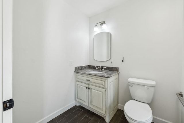 half bathroom featuring baseboards, vanity, toilet, and wood tiled floor