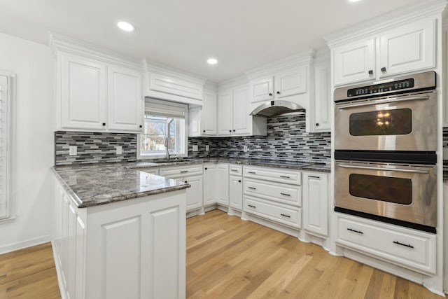 kitchen featuring white cabinets, stainless steel double oven, light wood-type flooring, under cabinet range hood, and a sink