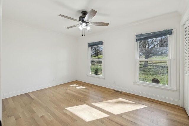 spare room featuring light wood-type flooring, a wealth of natural light, visible vents, and crown molding