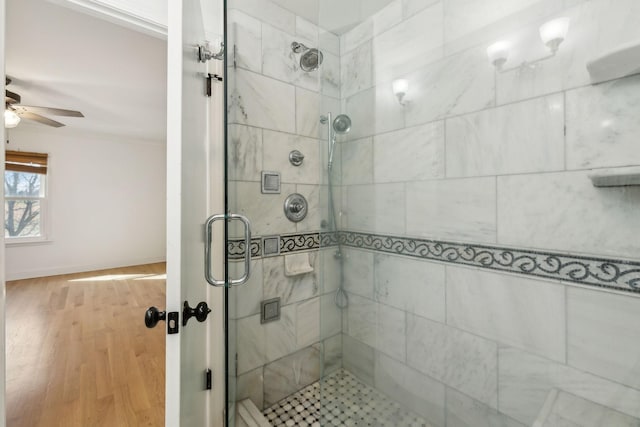 bathroom featuring ceiling fan, a stall shower, wood finished floors, and baseboards