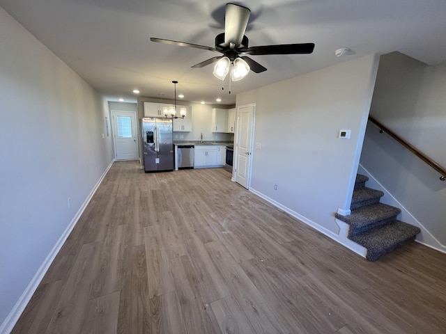 kitchen featuring stainless steel appliances, white cabinetry, baseboards, open floor plan, and light wood-type flooring