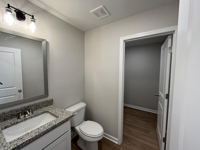 half bath with toilet, wood finished floors, vanity, visible vents, and baseboards