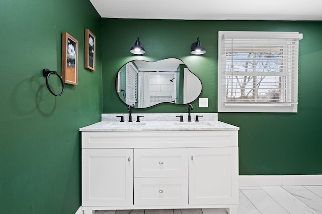 bathroom with double vanity, marble finish floor, baseboards, and a sink