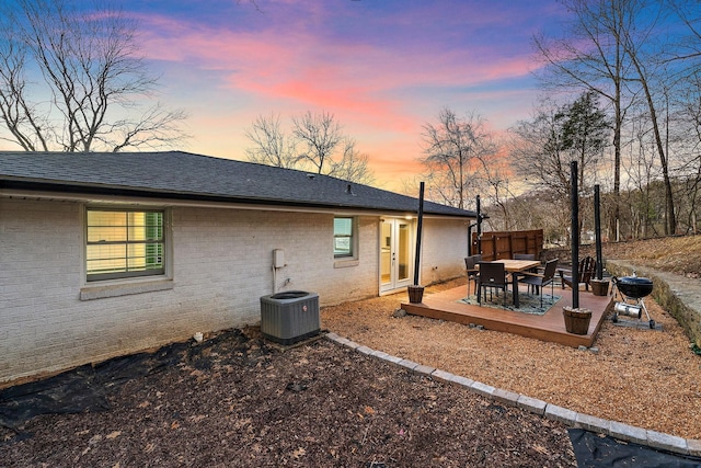 rear view of property featuring a deck, central AC unit, brick siding, a shingled roof, and fence