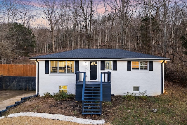 view of front facade with roof with shingles, fence, and brick siding