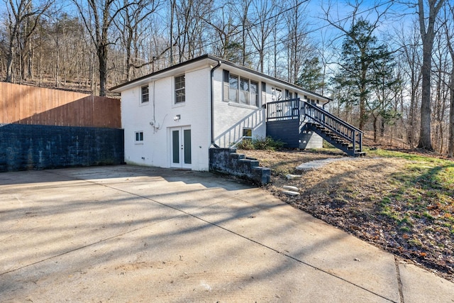 view of side of property featuring french doors, brick siding, concrete driveway, stairway, and fence