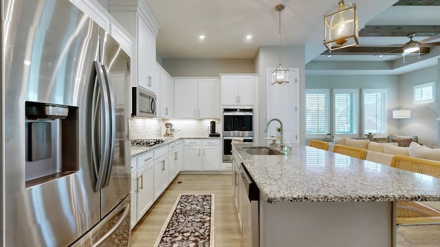 kitchen with stainless steel appliances, open floor plan, a kitchen island with sink, a sink, and light wood-type flooring