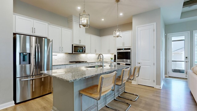 kitchen featuring decorative backsplash, appliances with stainless steel finishes, light wood-style floors, a sink, and light stone countertops