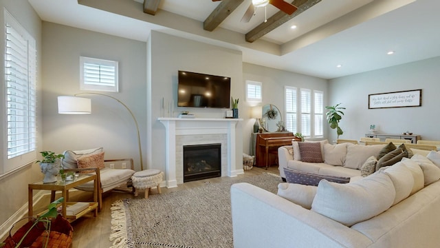 living area featuring light wood-style floors, a tile fireplace, beamed ceiling, and baseboards