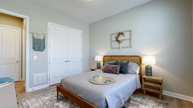 bedroom with a closet, visible vents, baseboards, and wood finished floors