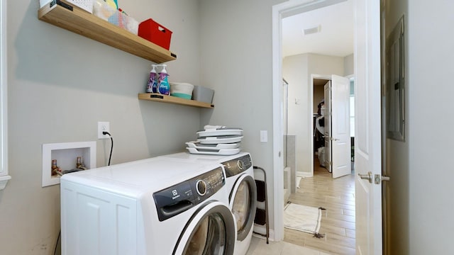 clothes washing area with washing machine and clothes dryer, visible vents, light wood-style floors, laundry area, and baseboards