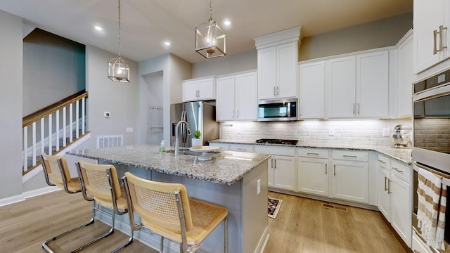 kitchen featuring appliances with stainless steel finishes, light stone countertops, light wood-type flooring, white cabinetry, and backsplash