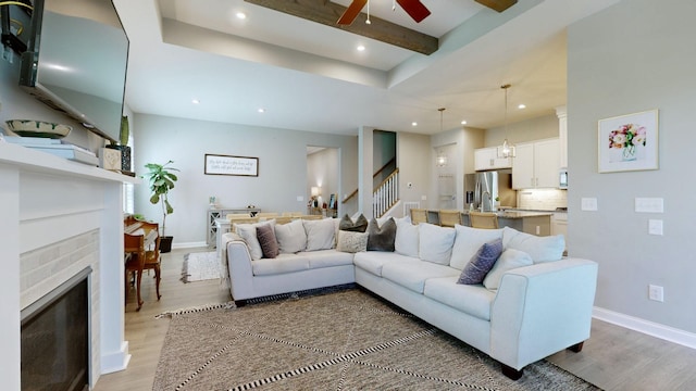 living room with baseboards, a fireplace, beam ceiling, and light wood-style floors