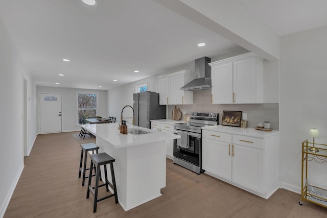 kitchen featuring appliances with stainless steel finishes, a kitchen island with sink, wall chimney range hood, a kitchen bar, and a sink