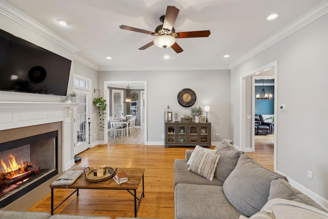 living area featuring a warm lit fireplace, recessed lighting, baseboards, ornamental molding, and light wood-type flooring