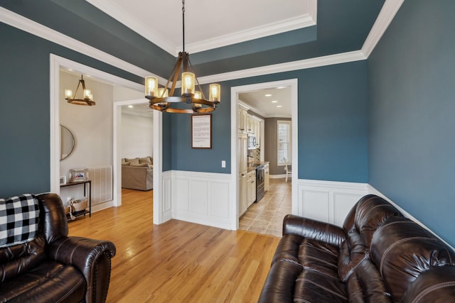 living room featuring light wood-type flooring, a wainscoted wall, crown molding, and an inviting chandelier