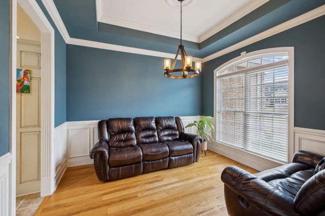 living room featuring light wood-style floors, wainscoting, a raised ceiling, and an inviting chandelier