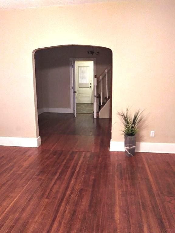 spare room featuring stairs, arched walkways, baseboards, and wood finished floors