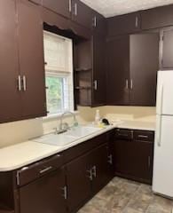 kitchen featuring dark brown cabinetry, light countertops, a sink, and freestanding refrigerator