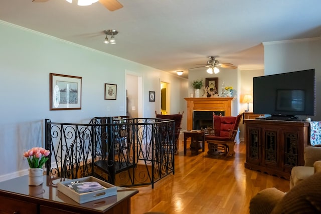 living room featuring crown molding, a fireplace, a ceiling fan, and wood finished floors